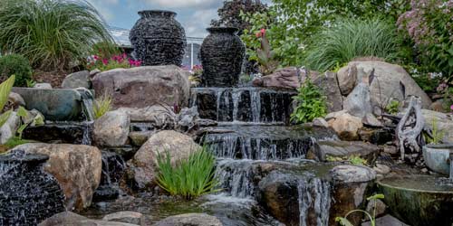 Custom Designed Water Feature With Rocks, Jugs, And Plants