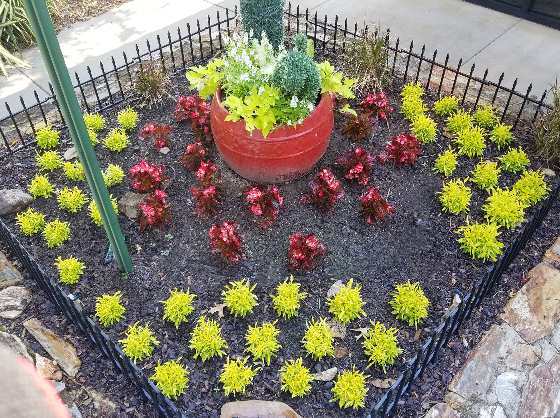 Stone Walled Garden Bed With Green And Red Plants And A Red Planter.