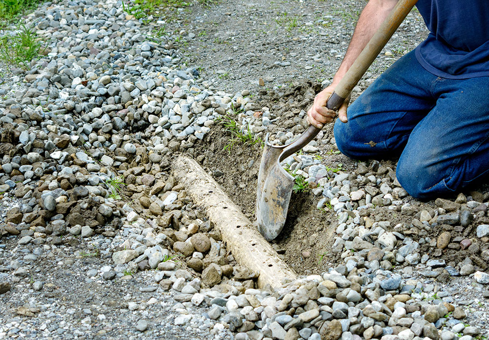 Man digging out french drain in driveway to clean out
